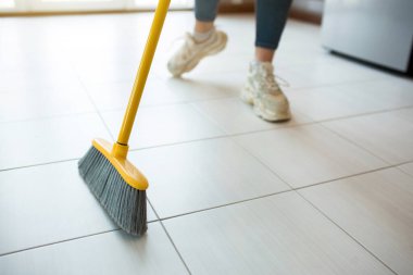 Karantina sırasında mutfakta genç bir kadın. Spor ayakkabılı bir kızın yeri tek başına süpürmesi. Ev mutfakta bekliyor. Gün ışığı.