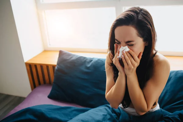 Young beautiful woman in morning bed at home. Blowing nose in white tisue. Flu or caught cold. Suffer from high temperature or virus. — Stock Photo, Image