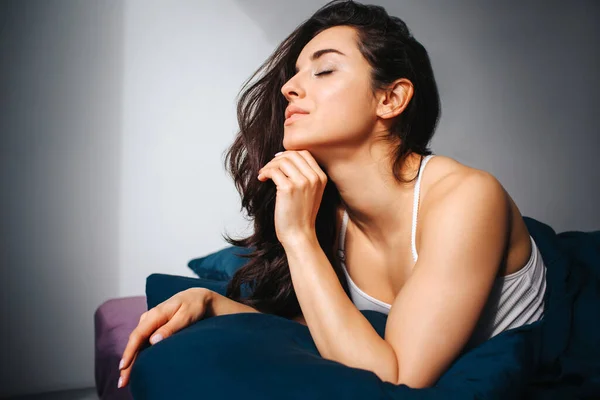 Young beautiful woman in morning bed at home. Dreamy sexy attractive female model posign with joy. Lying on bed with closed eyes and hold one hand under chin.