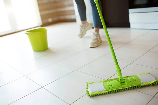 Ung kvinna i köket under karantänen. Rengöringsgolv med grön mopp. Låg sikt. Göra golvet mer rent. Grön hink med vatten bakom. — Stockfoto