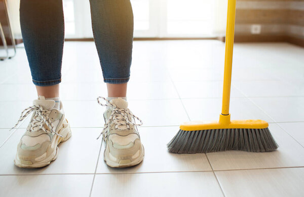 Young woman in kitchen during quarantine. Stand alone after sweeping floor. Hold broom with hand. Householding on free time.