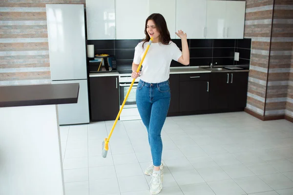 Young woman on kitchen during quarantine. Holding mop or broom in hand and singing out loud. Using cleaning equipment as microphone. After cwashing floor. — Stock Photo, Image