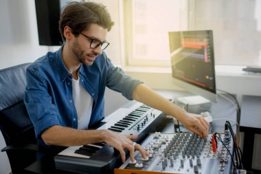 Müzik yapımcısı, kayıt stüdyosunda synthesizer klavye ve bilgisayar üzerine bir şarkı yazıyor. Adam kayıt stüdyosunda ses mikseri üzerinde çalışıyor ya da DJ yayın stüdyosunda çalışıyor.