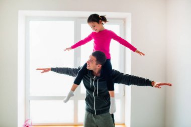 Genç baba ve küçük tatlı kızı evde antrenman yapıyorlar. Şirin çocuk ve babası içeride eğitim görüyor. Küçük siyah saçlı kadın model spor giyim bölümünde odanın penceresinin yanında egzersiz yapıyor.