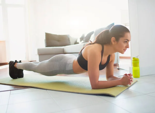 Ung kvinna gör sport träning i rummet under karantän. Sidovy av flicka stå på planka position med hjälp av underarmen kroppsdel på båda händerna. Rak välbyggd kaross. — Stockfoto