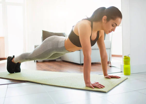 Ung kvinna gör sport träning i rummet under karantän. Koncentrerad lugn flicka står i planka position med händerna. Titta ner med koncentration. — Stockfoto