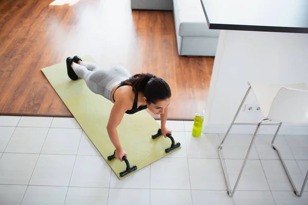 Ung kvinna gör sport träning i rummet under karantän. Upp sida vy av flicka stå i planka läge med hjälp av push up står handtaget. Motionera i rummet. — Stockfoto