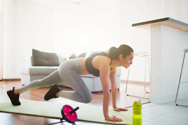 Mujer joven haciendo ejercicio deportivo en la habitación durante la cuarentena. Hacer ejercicio en la habitación en la esterilla de yoga. Párese en posición de tablón y y y haciendo ejercicio de escalador de montaje . — Foto de Stock