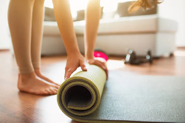 Ung kvinna som gör yoga träning i rummet under karantän. Klipp låg vy av barfota flicka rulla upp yogamatta efter avslutad stretching eller träning. — Stockfoto