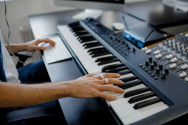 Kayıt stüdyosunda besteci elleri piyano tuşlarına basıyor. Müzik prodüksiyon teknolojisi, adam piyano ve bilgisayar klavyesi üzerinde çalışıyor. konsepti kapat.