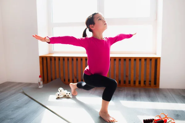 Liten flicka framåt lunge träning hemma. Söt unge tränar på en matta inomhus. Lite mörkhårig kvinnlig modell i sportkläder har övningar nära fönstret i sitt rum — Stockfoto