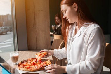 Kadın model elinde bir dilim pizza tutuyor. Pizza yiyen genç bir kadın.
