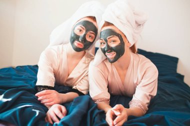 İki kadın model yüz maskesi yapıyor. Havlu ve pijamalı iki genç kadın evde eğlenceli bir spa partisi veriyor..