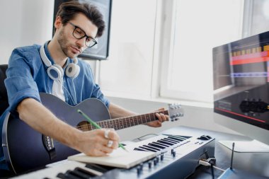 Dijital kayıt stüdyosunda Midi piyano ve ses ekipmanları besteleyen erkek müzik düzenleyicisi. İnsan gitar çalar ve projede elektronik soundtrack veya parça üretir..