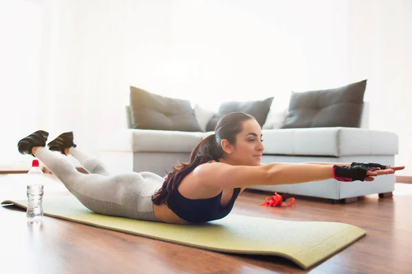 Ung kvinna gör sport träning i rummet under karantän. Ligger på mattan och håller fram med händerna. Hemmaträning utan utrustning. — Stockfoto