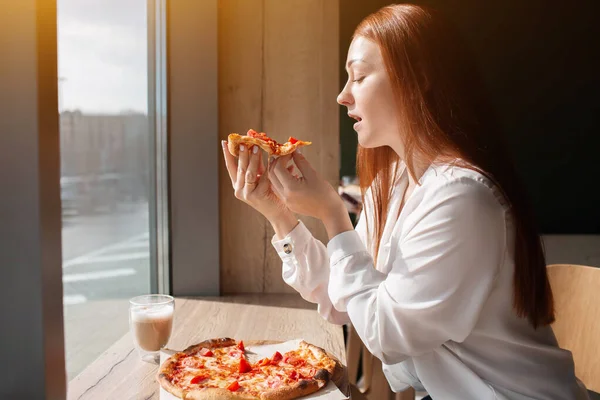 Kadın model elinde bir dilim pizza tutuyor. Kafede pizza yiyen genç bir kadın.. — Stok fotoğraf