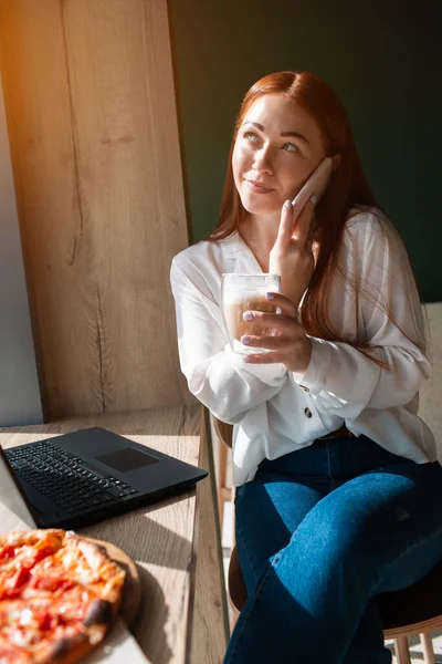 Жіноча модель розмовляє по телефону і п'є каву. Молода жінка сидить у кафе . — стокове фото