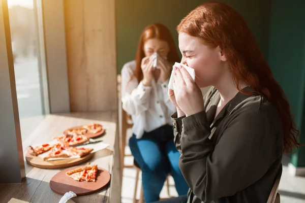 Young women blow nose in a napkin. Female models are sitting in a cafe and wipe nose.