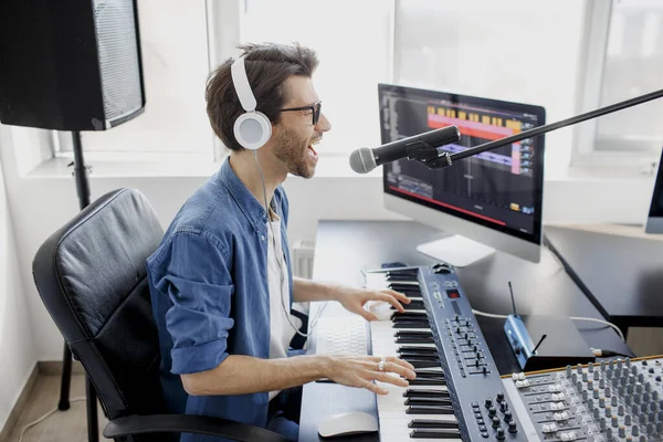 Man plays guitar and singing and produce electronic soundtrack or track in project at home. Male music arranger composing song on midi piano and audio equipment in digital recording studio