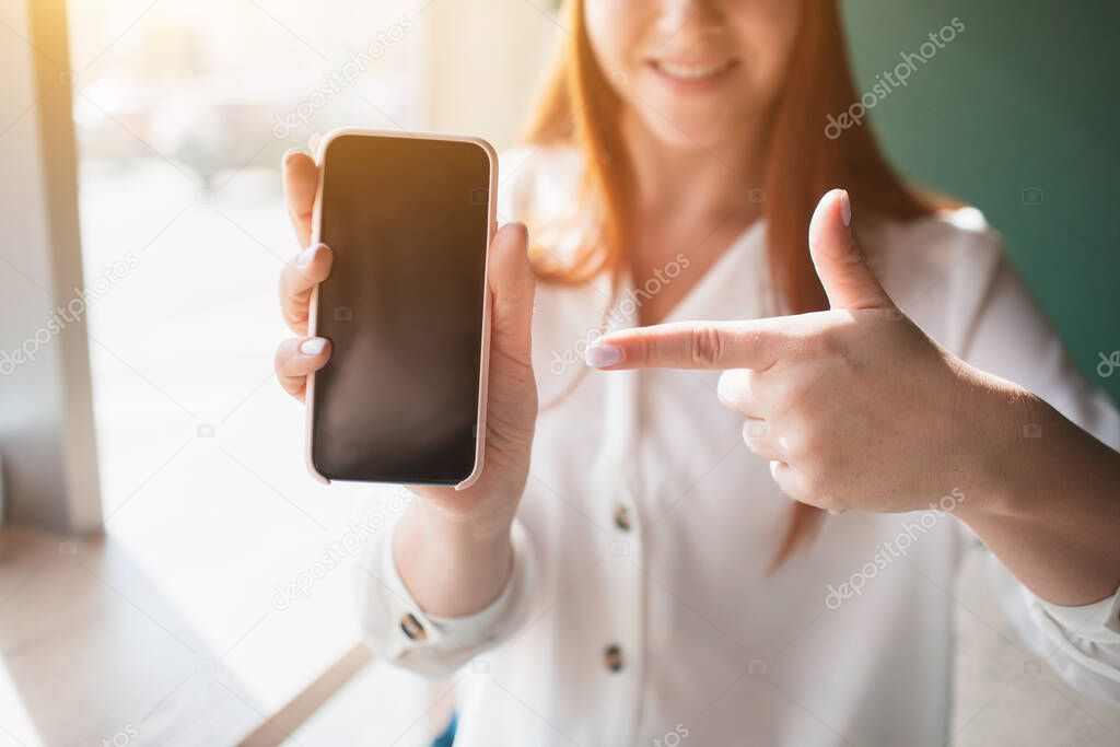 Index finger points at the phone close-up. Young woman holds and uses a smartphone in her hands.