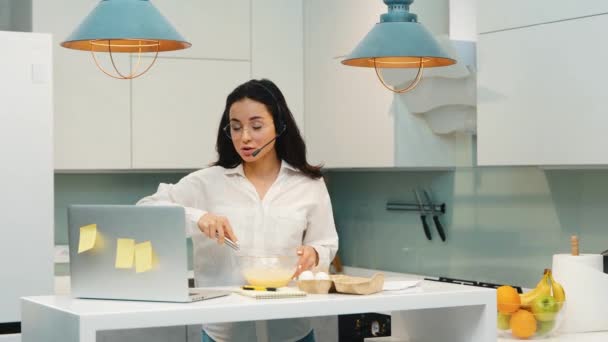 Mladá žena pracuje doma během karantény. Help desk girl operator talking on video call and preparing breakfast. Multitasking a multifunkční zaměstnanec. — Stock video