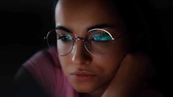 Young woman at home during quarantine. Close up of girl in glasses looking on screen. Reflection of video playing. satisfied happy woman watching video. — Stock Video