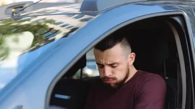 Arabanın içindeki genç adam. Ağır çekimde adam çok kötü ve sert bir şekilde yakıyor. Ağzını elinle kapat. Koronavirüs semptomlarından muzdarip..