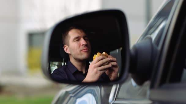 Arabanın içindeki genç adam. Yan aynada, tişörtlü adamın hamburger yediği bir manzara. Kahvaltı ya da arabada öğle yemeği. Yemek yemek ve eğlenmek. Yavaş çekim. — Stok video