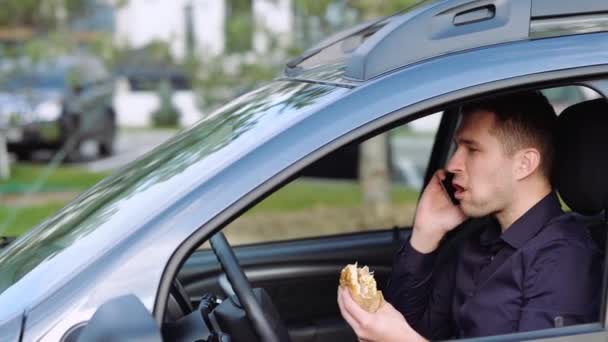 Giovanotto in macchina. Parlare al telefono e mangiare hamburger. Un altro arriva in macchina e inizia a litigare. Uomo d'affari in auto d'accordo e guidare via . — Video Stock