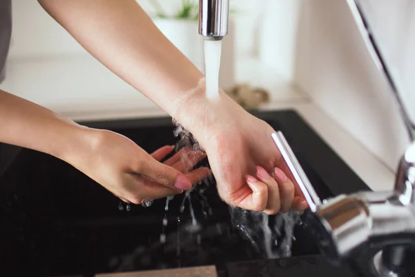 Young woman in kitchen during qiarantine. Cut view of gorls hands holding under water jet come out of tap. Washing or warmiing up hands and wrist. — Stock Photo, Image