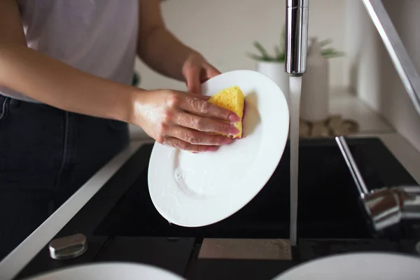 격리되어 있는 동안 부엌에 있던 소녀. 스폰지와 식기세척기가 달린 흰 접시를 만드는 일. 부엌에서 혼자 설거지를 한다. 컷 뷰. — 스톡 사진