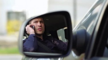 Arabanın içindeki genç adam. İş adamlarının telefonda konuşmaları ve tartışmaları yavaş ilerliyor. Dikiz aynasında ciddi konsantre bir adam..