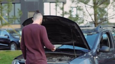 Arabanın dışındaki genç adam. Kaputunu aç ve bozuk motorla çaresiz. Yardım ve yardım için telefonla aranıyor..