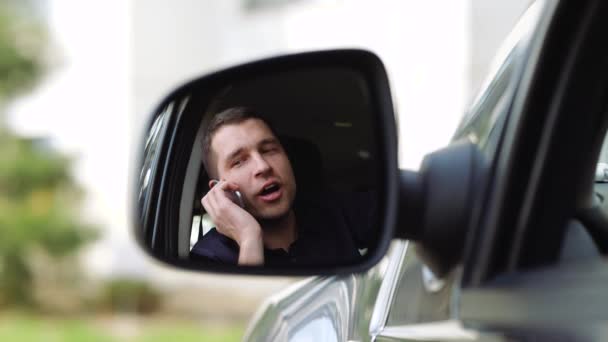 Unge man i bilen. En vy från sidospegel av affärsman som pratar i telefon. Ha ett trevligt samtal. Företagssamtal. — Stockvideo