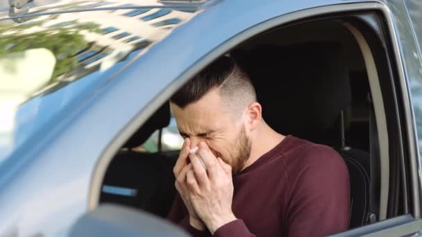 Unge man i bilen. Killen lider av nysningar och fruktansvärd huvudvärk. Sitt ensam med symtom på coronavirus. Nysningar i vit vävnad. — Stockvideo