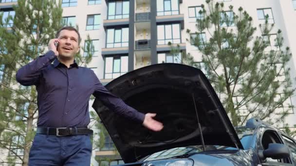 Giovanotto in macchina. Un tizio che spiega problemi con un'auto rotta. Stand besdies cappuccio aperto. Bisogno di aiuto e assistenza . — Video Stock