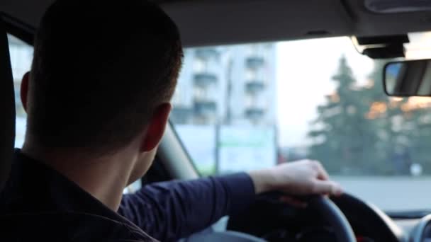 Jongeman in de auto. Vrolijke positieve knappe bestuurder zit op de voorbank, kijk achterom en glimlach. Handen vast aan het stuur. — Stockvideo