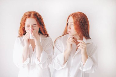 Mendilli genç bir kadın. Hasta kızın burnu akıyor. Kadın model, beyaz arka planda izole edilmiş soğuk algınlığına çare bulur. İkinci genç kadın enfeksiyon kapmaktan korkuyor.