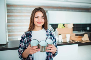 Genç bir aile geridönüşüm için malzemeyi mutfakta sınıflandırıyor. Geri dönüşümlü materyaller ayrılmalı. Yaşlı teneke kutuları yiyecek için elinde tutan genç bir kadın. Arka planda çöp kutuları var..