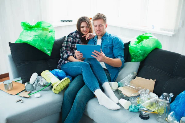 Environmental pollution concept. Silin young couple on the sofa in the living room. There is a lot of rubbish, plastic waste around. People do not notice problems with plastic pollution