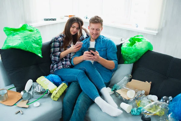 Environmental pollution concept. Silin young couple on the sofa in the living room. There is a lot of rubbish, plastic waste around. People do not notice problems with plastic pollution — Stock Photo, Image