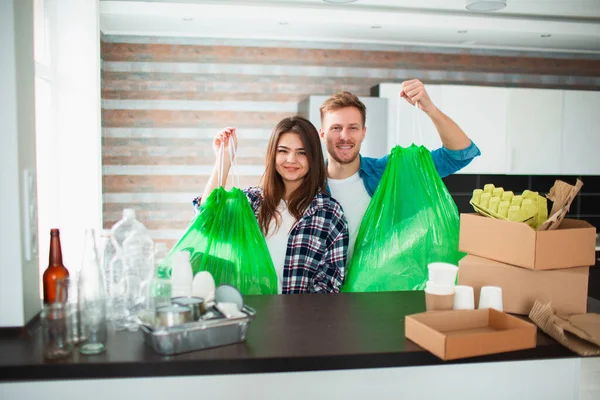 Couple sorts trash in the kitchen. Waste must be sent for recycling. There are a lot of recyclables. On the table are plastic, glass, iron, paper, old Electrical appliances and biodegradable waste.