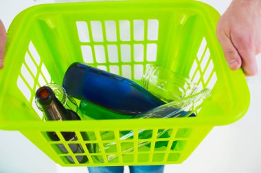 Genç adam beyaz arka planda izole edilmiş. Yaklaş ve yeşil plastik sepeti tutan elleri kes. İçinde renkli cam şişeler var. Geri dönüşüm zamanı ve atık yaşam tarzı yok.