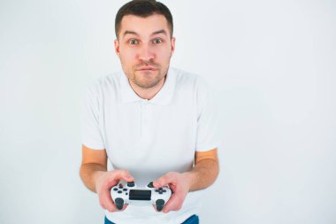 Genç adam beyaz arka planda izole edilmiş. Oyuncu elinde joystickle oynar. Yoğun bir oyun. Yoğunlaşmış adam önüne bak. Karantina sırasında oynamak.