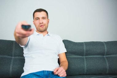 Genç adam karantina sırasında odada oturur. Uzaktan kumanda kullanan bir adam bir elinde tutuyor. Adam tek başına oturup televizyon kanallarını değiştiriyor..