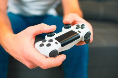 Genç adam karantina sırasında odada oturur. Görüntüyü kesin ve joystick ya da oyun platformunu elinizde tutarken ellerinizi kapatın. Düğmelere basıp oynuyorum. Bulanık arkaplan.