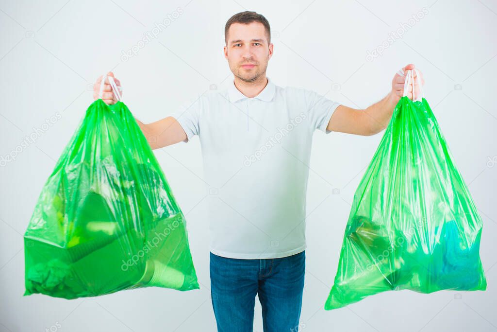 Young man isolated over white background. Guy hold two plastic bags with trash and waste inside it. Getting ready for resycling and reusing process.