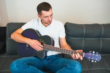 Genç adam karantina sırasında odada oturur. Adam akustik gitar çalıyor. Yalnız öğreniyorum. Parmaklarını tellere dola ve çal. Filmdeki müzisyen.