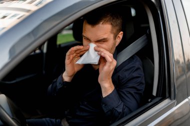 young man with handkerchief. Sick guy has runny nose. Male model makes a cure for the common cold in the car. clipart