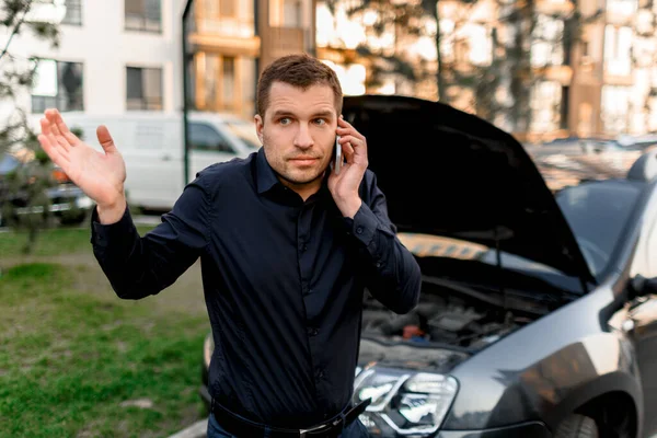 Car breakdown concept. The car will not start. A young man is calling for a car service. They cannot fix the car on their own. Insurance must cover all costs.